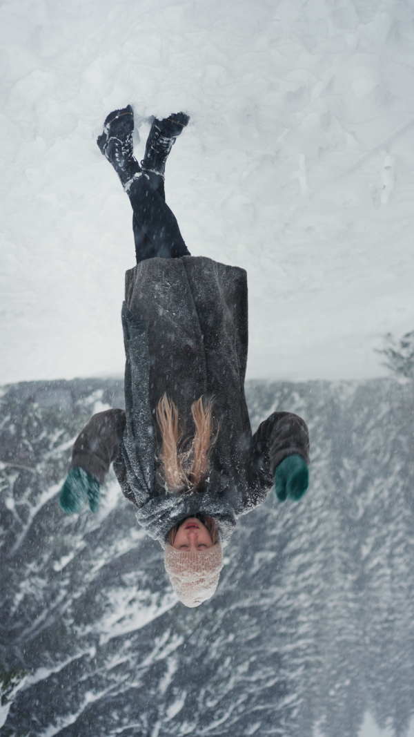 A happy young woman in winter under falling snow in nature looking at camera, vertical footage.