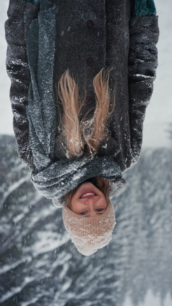 A happy young woman in winter under falling snow in nature looking at camera, vertical footage.