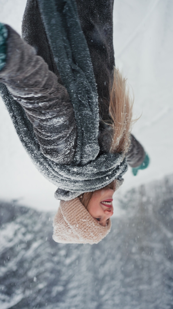 A vertical footage of happy young carefree woman breathing fresh air in the snowy nature.