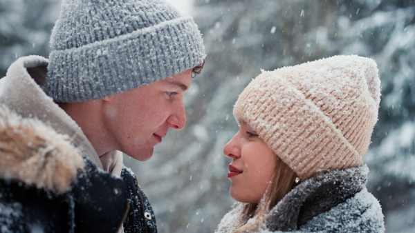 A close-up of young couple hugging and kissing in winter under falling snow in nature.