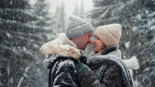 A close-up of young couple hugging and kissing in winter under falling snow in nature.