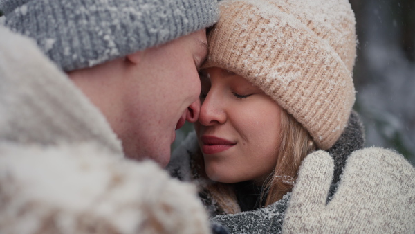 A close-up of young couple hugging and kissing in winter under falling snow in nature.