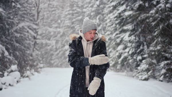 A young man in winter under falling snow in nature.