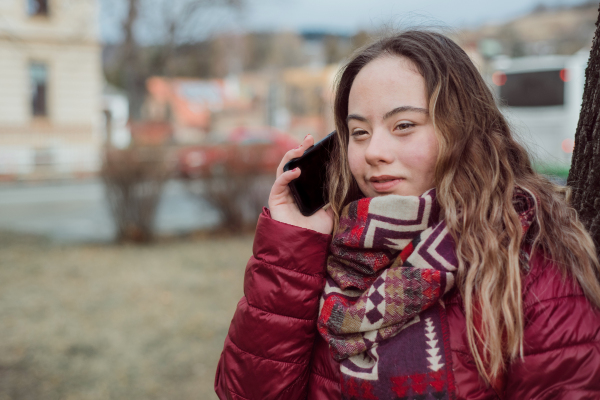 A young woman with Down syndrome walking in street in winter and using smartphone