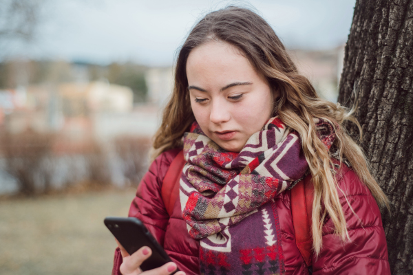 A young woman with Down syndrome walking in street in winter and using smartphone