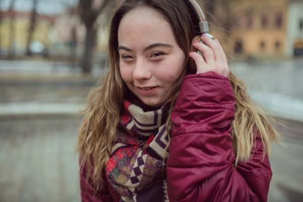 A happy young woman with Down syndrome listening to music in town in winter