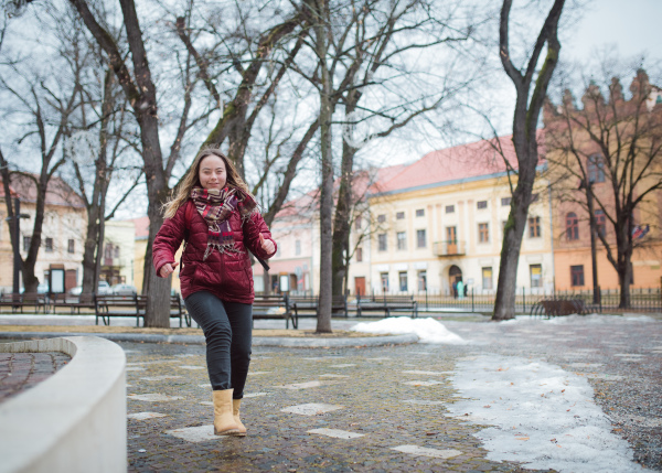 A happy young woman student with Down syndrome running in street in winter