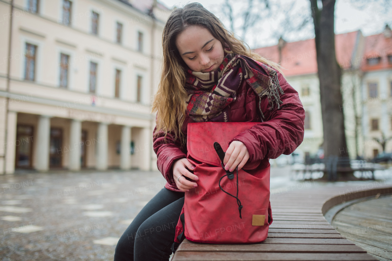 A young woman with Down syndrome sitting on bench and resting in town in winter