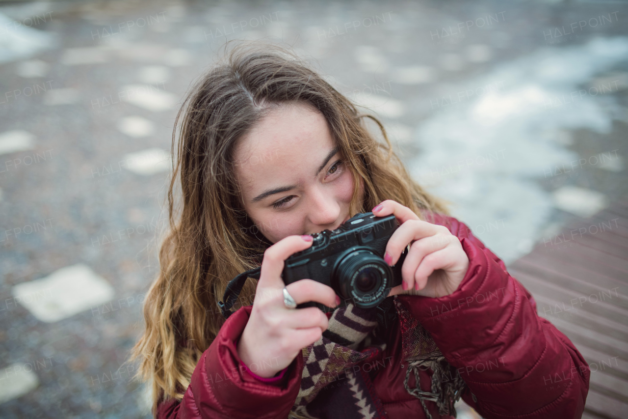 A young woman with Down syndrome using camera in town in winter and looking at camera.