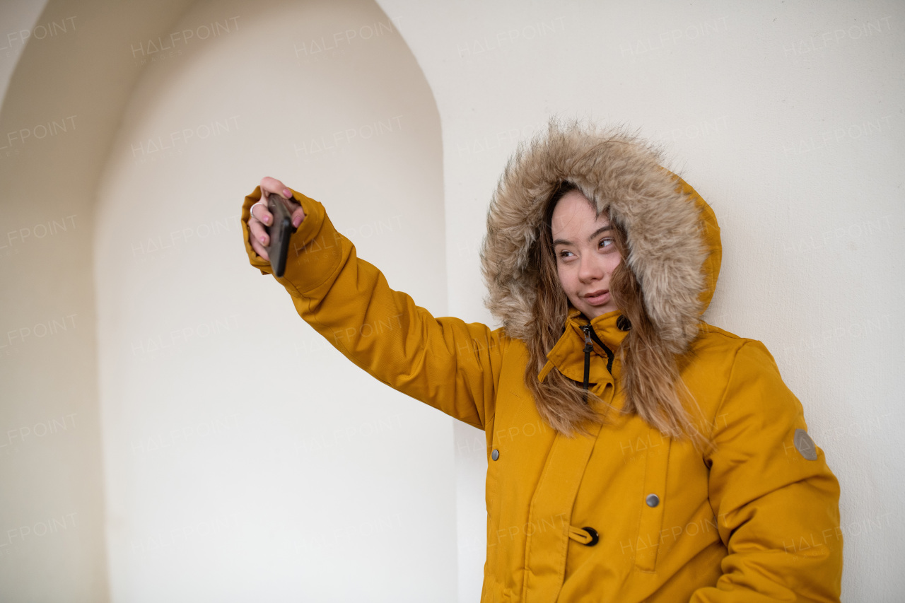 A happy young woman with Down syndrome taking selfie in town in winter.