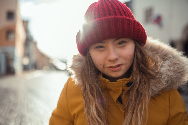 A happy young woman with Down syndrome weraing parka and hat, walking in town and looking at camera.