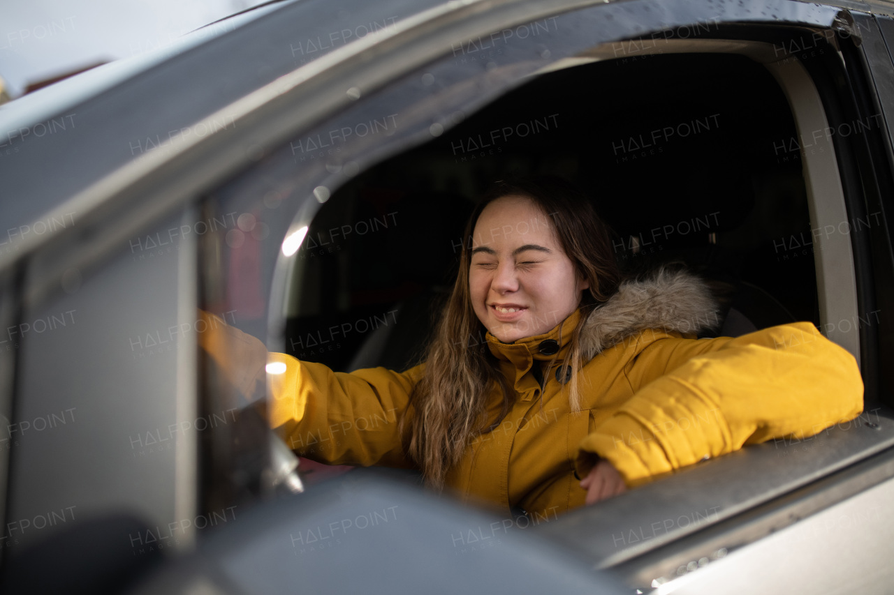 A young woman with Down syndrome driving a car and smiling.