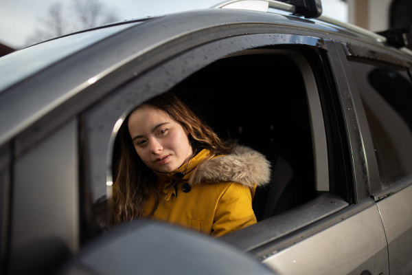 A young woman with Down syndrome driving a car and looking at camera.