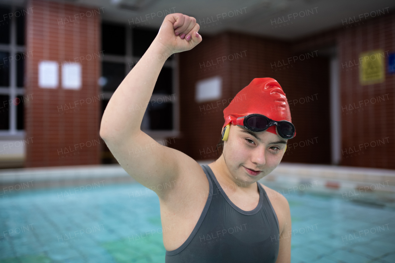 A young woman with Down syndrome inm swimming pool raising arm and looking at camera