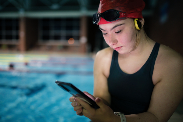 A young woman with Down syndrome in swimming pool using smartphone