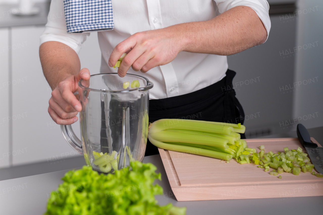 An unrecognizable man putting cellery to blender to make fresh homemade smoothie. Healthy lifestyle concept