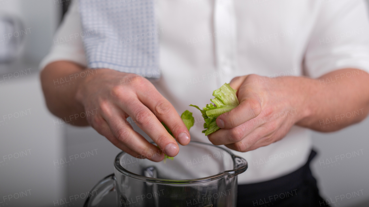 An unrecognizable man putting lettuce to blender to make fresh homemade smoothie. Healthy lifestyle concept