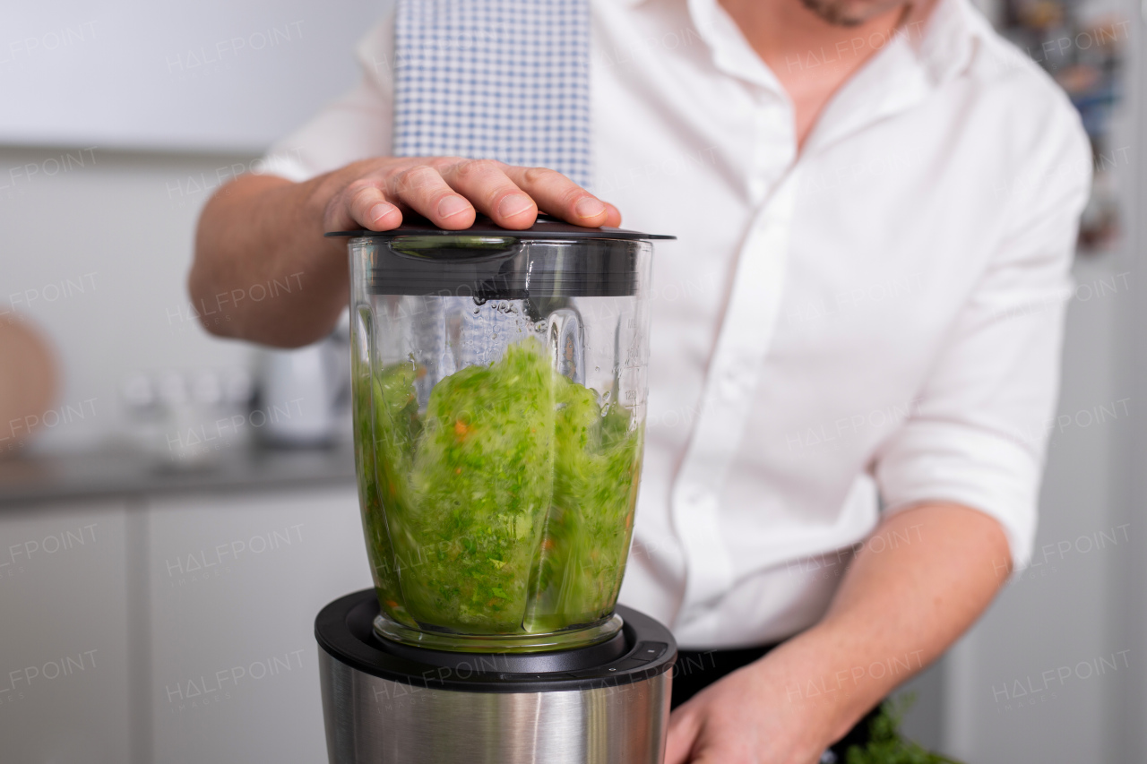 An unrecognizable man making green homemade smoothie in blender. Healthy lifestyle concept.