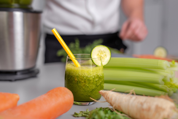 A green smoothie in glass with straw and cucumber and vegetagbles at background, detox, vegan, vegetarian healthy vegetable drink