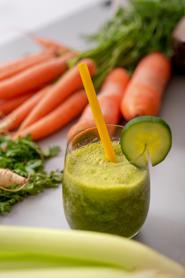 A green smoothie in glass with straw and cucumber and vegetagbles at background, detox, vegan, vegetarian healthy vegetable drink