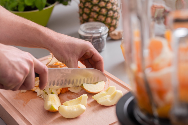 An unrecognizable man cutting apples on chopping board.