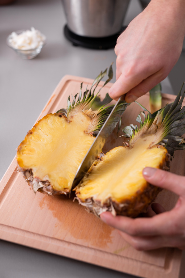 An unrecognizable man cutting a pineapple on chopping board.