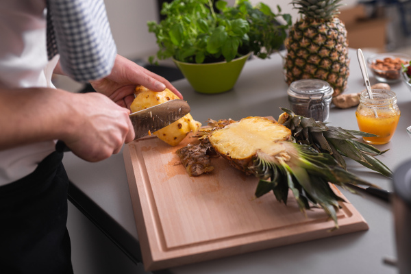 A man standing behind bar counter cutting a pineapple on chopping board.