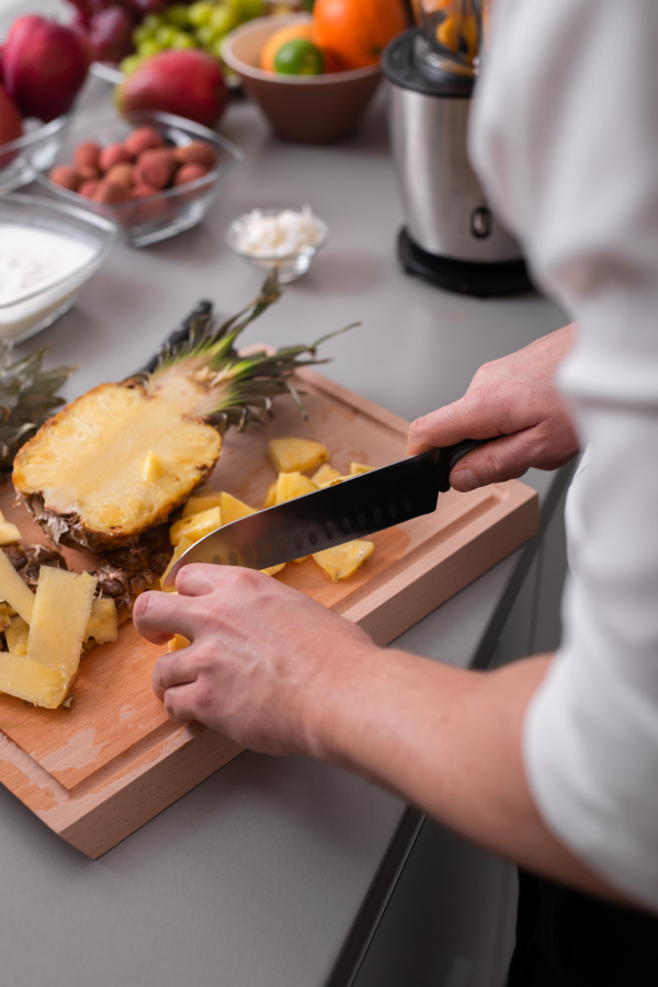 An unrecognizable man cutting a pineapple on chopping board.