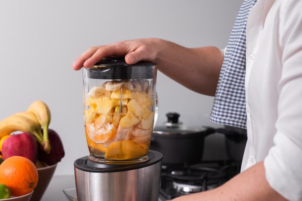 A close up cropped shot of man making smoothie from fresh fruits in professional blender or food processor.