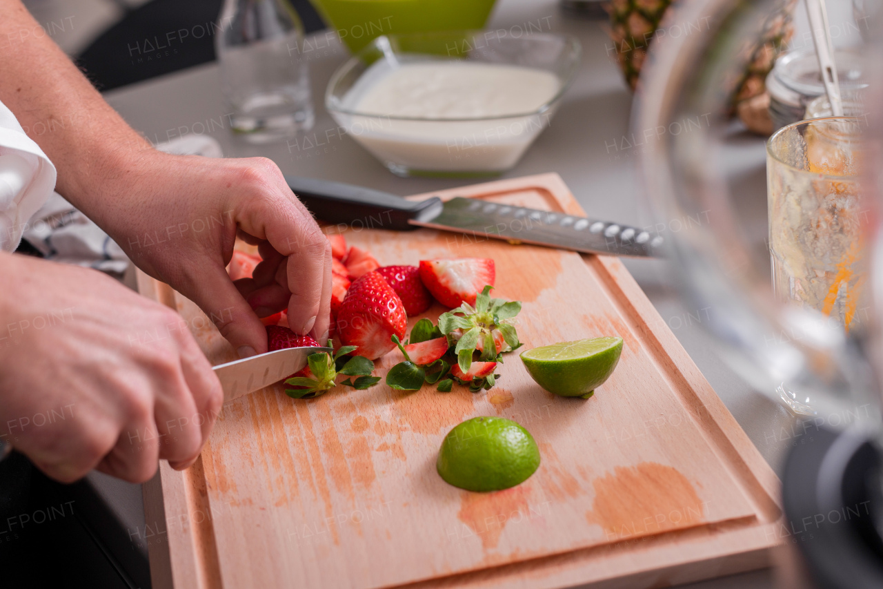 A man cutting strawberries and limes on chopping board.