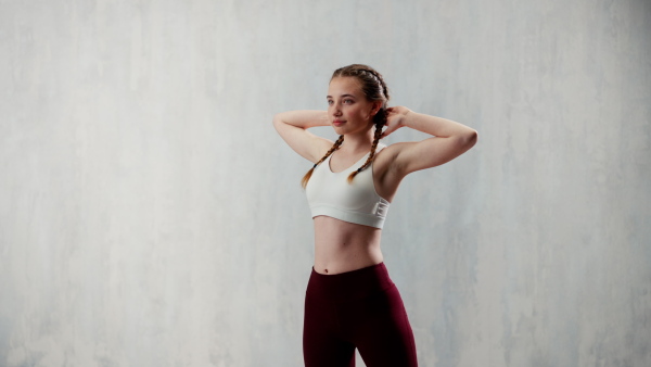 A young sporty woman in sports clothes stretching arms against beige background, copy space