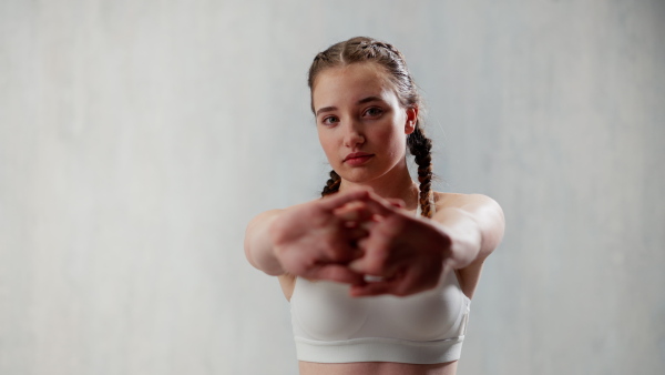 A young sporty woman in sports clothes stretching arms against beige background, copy space