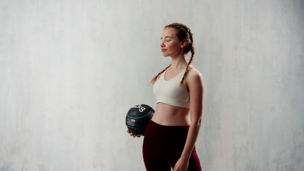 An athletic fitness woman working out with medicine ball on grey background. Copy space.