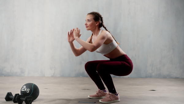 A sports woman in fashion black sport clothes squatting doing sit-ups in gym, over gray background