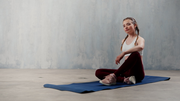 A sports woman in fashion sport clothes working out against grey wall, doing yoga, pilates balancing exercise.