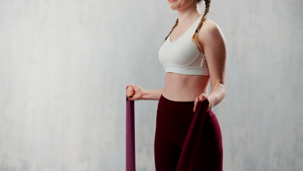 A sports woman in fashion sportswear exercising with elastic band stretch over greay background.