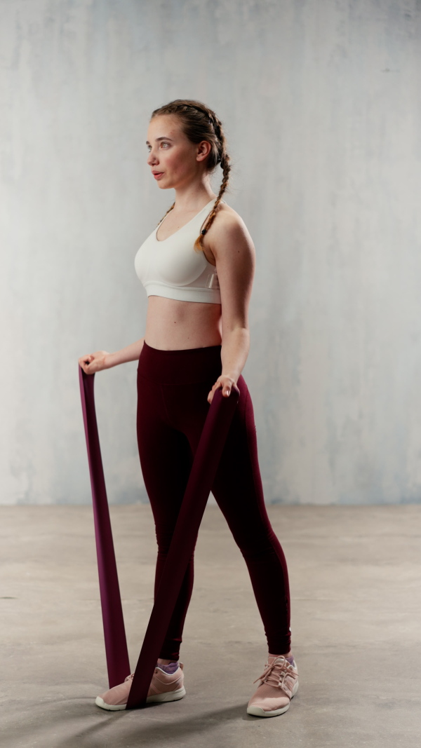 A sports woman in fashion sportswear exercising with elastic band stretch over greay background.