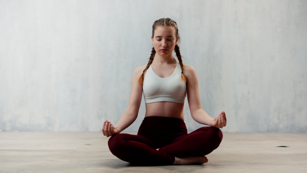 A young healthy woman in black sportsclothes practising yoga in studio, in a yoga position, copy space