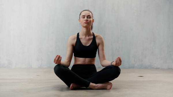 A young healthy woman in black sportsclothes practising yoga in studio, in a yoga position, copy space