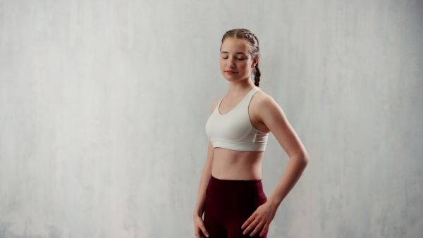 A vertical footage of sports woman in fashion sport clothes posing in gym, over gray background