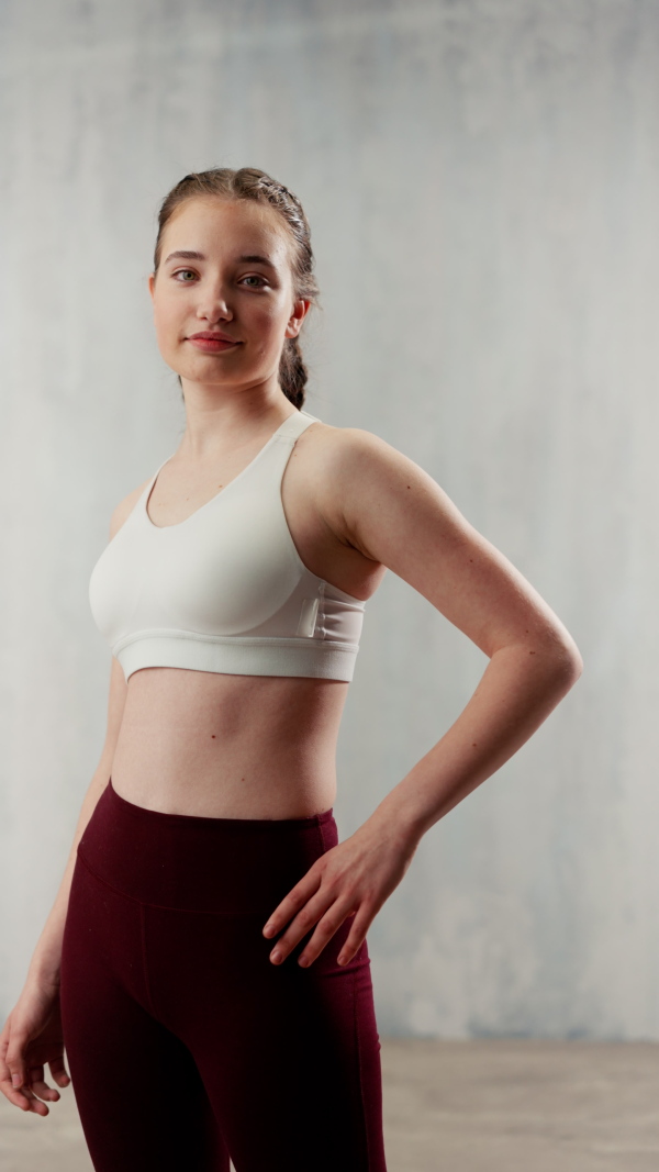 A vertical footage of sports woman in fashion sport clothes posing in gym, over gray background