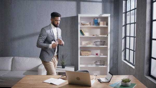 A young african american businessman strating work on laptop after break on sofa indoors in office