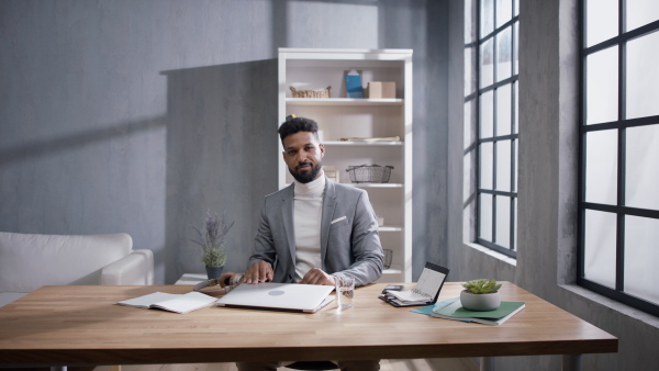 A happy young multiracial businessman finished his work on laptop indoors in office, looking at camera