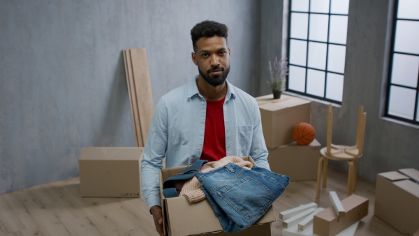 A happy young man holding packing boxes moving home, looking at camera, new living concept.