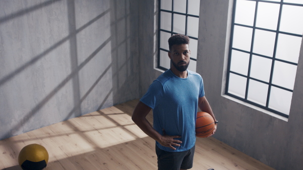 A young African American basketball player standing indoors at gym, looking at camera.