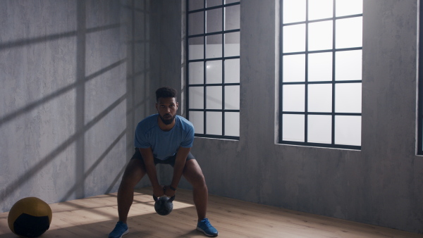 A young African American sportsman standing and lifting a kettle bell indoors, workout training concept.