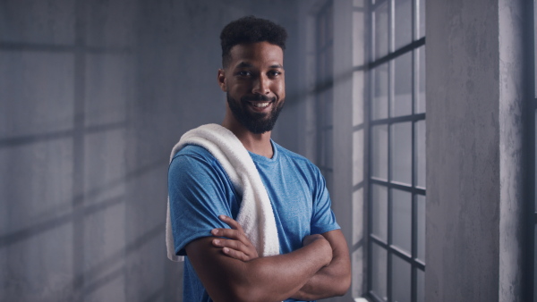 Portrait of a happy young African American sportsman standing indoors at gym, looking at camera, workout training concept.