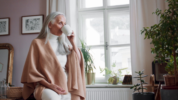 A fashionable senior woman sitting on table and drinking coffee at home.