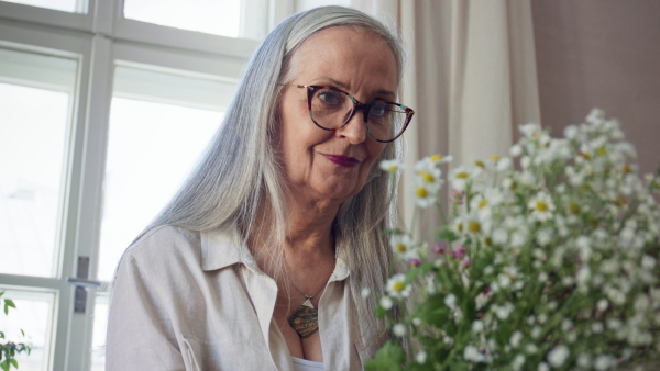 A happy senior woman taking care of plants indoors at home.