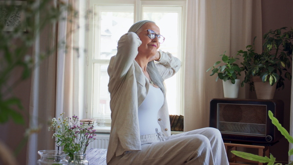 A senior woman sitting on table and stretching indoors at home.